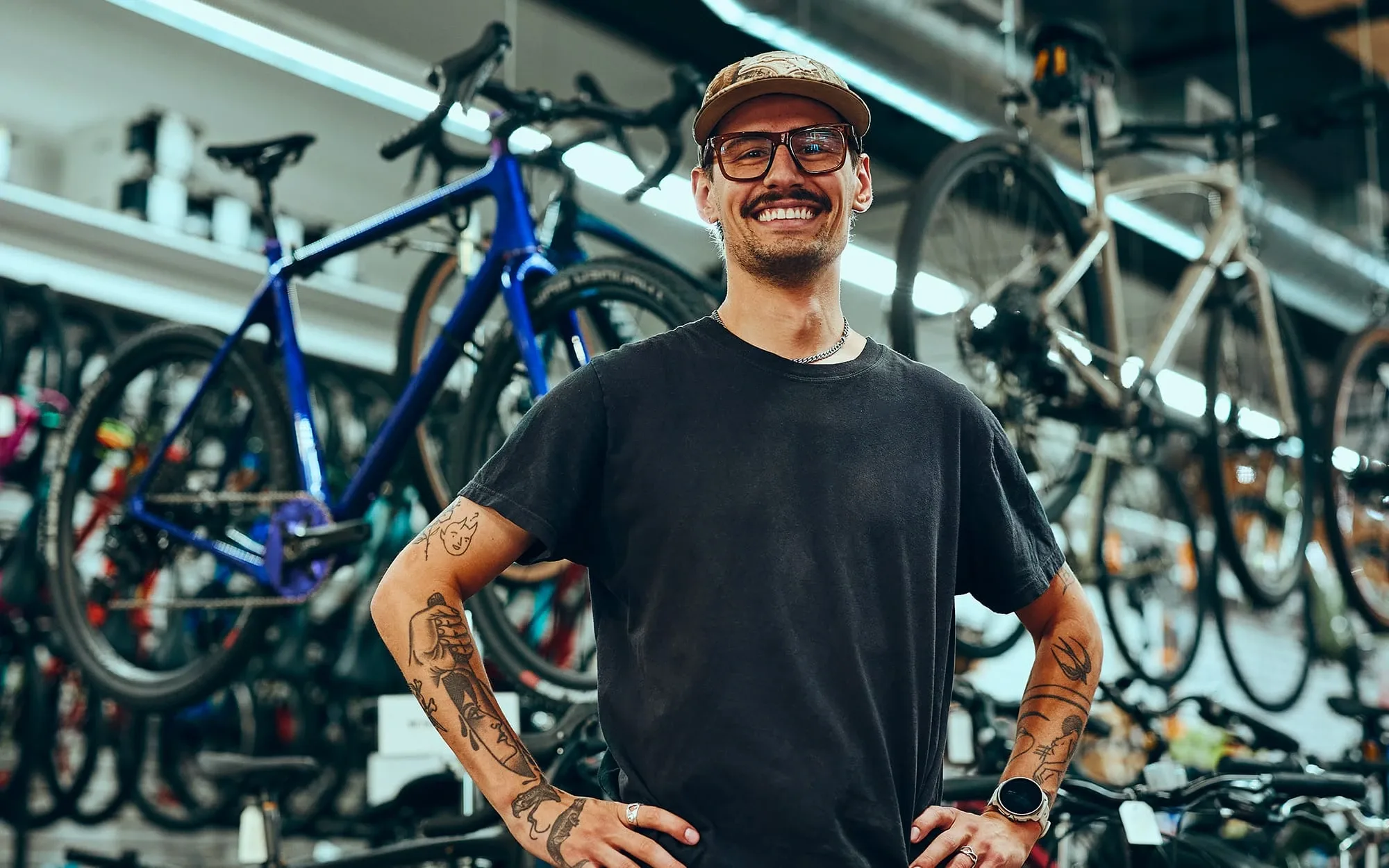 Homme souriant avec des lunettes qui se tient devant beaucoup de vélos dans un entrepôt